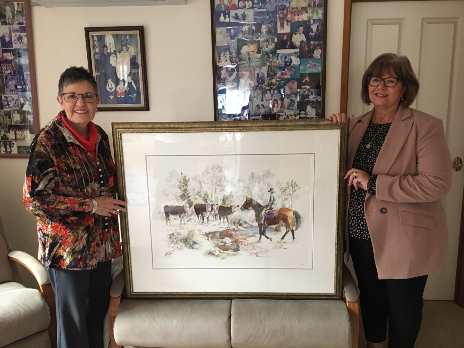 Two women hold a painting that features a cattleman on horseback.